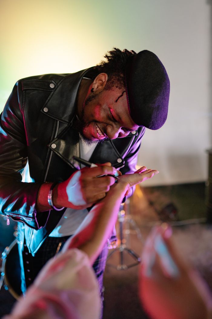 our-mission A smiling musician in a black leather jacket signing autographs at a concert.